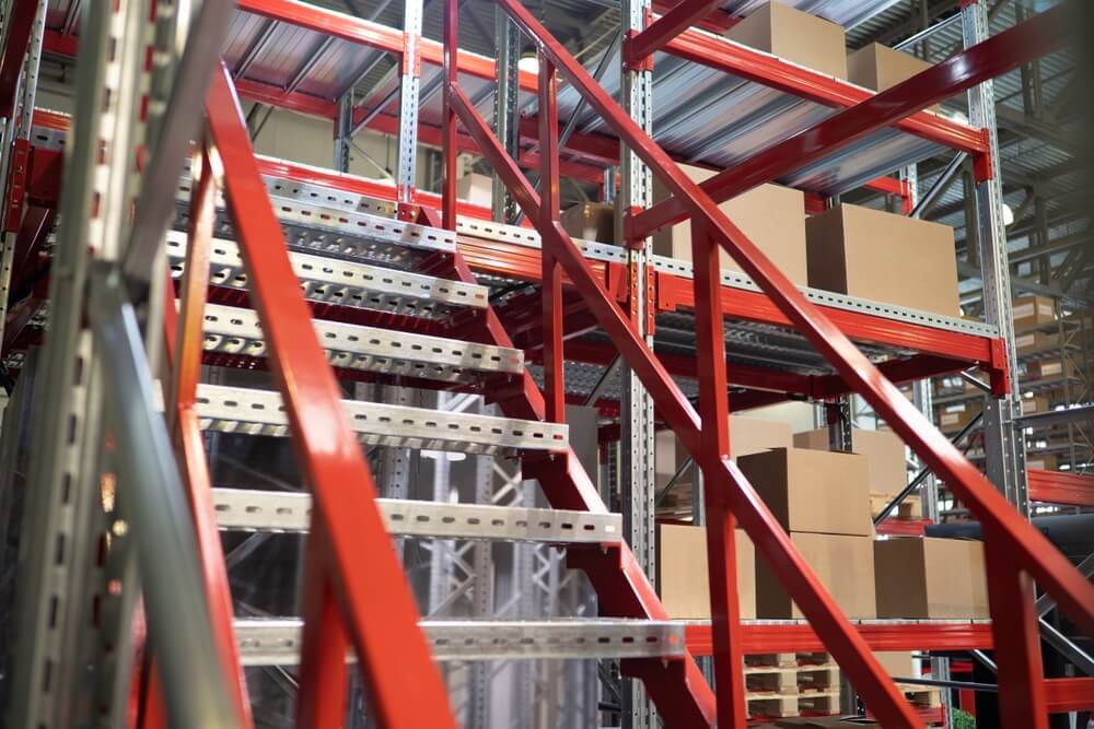 Industrial mezzanine platform with red steel stairs and shelving, used for elevated storage and organization in a warehouse.