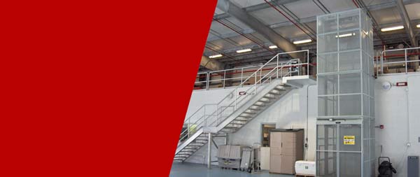KABTech's Vertical Material Lift Next To A Set of Stairs in a Warehouse
