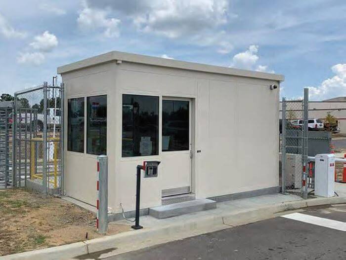 A security booth at the gates of an industrial facility with a security keypad system next to it.