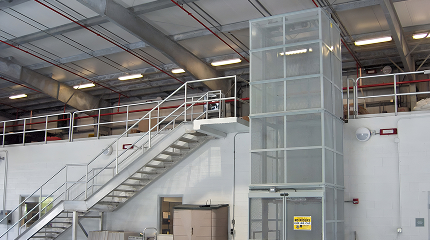 KABTech's Vertical Material Lift Next To A Set of Stairs in a Warehouse